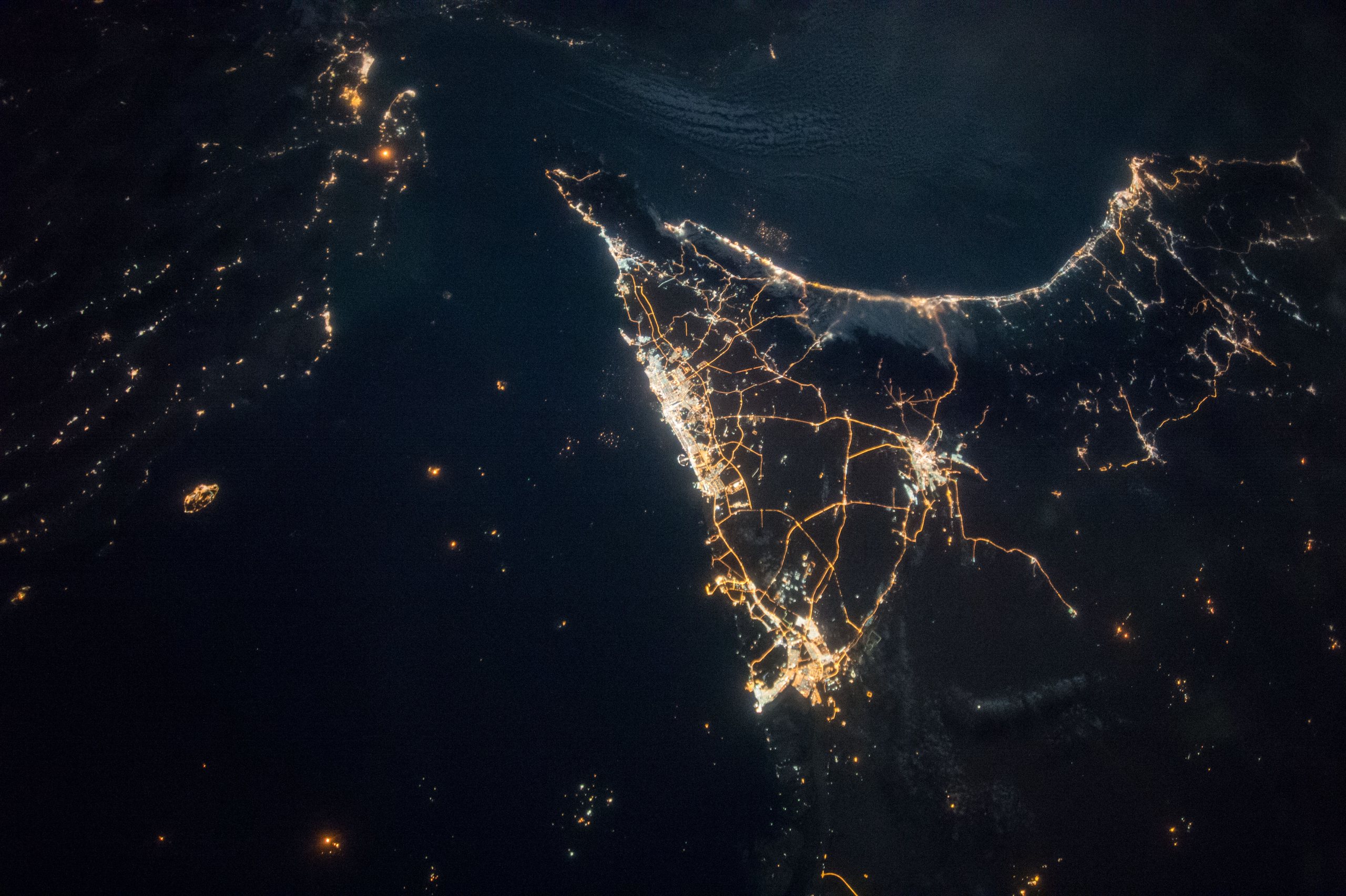 The United Arab Emirates at night seen from orbit, its cities and highways lit in gold along the dark Gulf coast.
